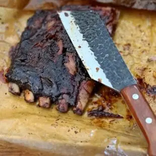 BBQ-kniv Kockkniv BBQmonster - robust kniv/cleaver med slida i läder. 5mm grov rygg och en vikt på 400 gram En bbq-kniv för BBQ och Grillning: BBQmonster BBQ-kniv / cleaver är kniven som är en kombination av en rejäl kockkniv och en Cleaver / köttyxa, och med denna i din hand är inte en kotlettrad eller ett revbensspjäll säkert någonstans. Bladet är EXTREMT stabilt och viker inte även vid hårdare tag. Ryggen är hela 5mm tjockt och större delen av bladet har en härlig hammrad yta som kniven rejält "intstagramvänlig" och photogenique. Denna BBQkniv kommer en slida av läder vilket gör att du kan bära den i din livrem eller i ditt förkläde. Skaftet är av polerat och lackat hårdträ och detta omsluter det genomgående knivbladet avslutning. Skaftet ger ett bra grepp och är enkelt att rengöra. Handtaget passar både höger- och vänsterhänta. Kolstål med blandning X50CrMoV15 Hårdhet 56° HRC vilket är ett relativt mjukt stål - något som gör att du själv enkelt kan hålla din kniv vass. Total längd: 29 cm Längd på bladet: 18 cm Längd på skaftet: 11 cm