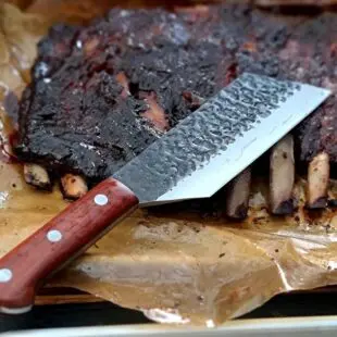 BBQ-kniv Kockkniv BBQmonster - robust kniv/cleaver med slida i läder. 5mm grov rygg och en vikt på 400 gram En bbq-kniv för BBQ och Grillning: BBQmonster BBQ-kniv / cleaver är kniven som är en kombination av en rejäl kockkniv och en Cleaver / köttyxa, och med denna i din hand är inte en kotlettrad eller ett revbensspjäll säkert någonstans. Bladet är EXTREMT stabilt och viker inte även vid hårdare tag. Ryggen är hela 5mm tjockt och större delen av bladet har en härlig hammrad yta som kniven rejält "intstagramvänlig" och photogenique. Denna BBQkniv kommer en slida av läder vilket gör att du kan bära den i din livrem eller i ditt förkläde. Skaftet är av polerat och lackat hårdträ och detta omsluter det genomgående knivbladet avslutning. Skaftet ger ett bra grepp och är enkelt att rengöra. Handtaget passar både höger- och vänsterhänta. Kolstål med blandning X50CrMoV15 Hårdhet 56° HRC vilket är ett relativt mjukt stål - något som gör att du själv enkelt kan hålla din kniv vass. Total längd: 29 cm Längd på bladet: 18 cm Längd på skaftet: 11 cm