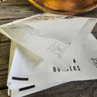 Hamburgarfickor vita "keep calm and eat burgers" BBQmonster 100st - undvik dressing längs underarmarna med en hamburgerficka Hamburgerfickor i BBQmonsters egna design i tilltagen storlek. Tåligt papper med glättad (vaxad) insida förhindrar att fett och dressing läcker igenom. I dessa snygga burgarfickor / hamburgarfickor som säljs i ett prisvärt 100pack virar in din burgare i eller som du stoppar dina pommes i. Burgarfickorna är förseglade i två av de fyra sidorna och är enkla att öppna då baksidan är 1cm större än framsidan Praktiskt - en hamburgerficka förhindrar att du grisar ner dig allt för mycket, för vem njuter av dressing rinnande längs med underarmarna? Är du ute efter den autentiska stilen som förhöjer känslan av en #Burgerlifestyle ? Då är dessa hamburgarefickor bara ett måste. 16x16cm (framsidan 15cm för enklare öppning av fickan) 100-pack Lätt vaxat Coolt tryck på båda sidorna (olika motiv fram respektive bak) Höjd: 16 cm Bredd: 16 cm Tips: spana in vår nya mini-bricka i aluminium för servering av burgare, hamburgare och smashburger: