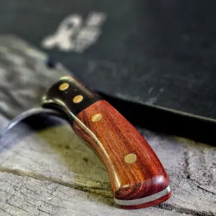 Kökskniv / Cleaver "Fire #7" 29cm - grovt kolstål med fina detaljer och galet vass - med ölöppnare på ovansidan av bladet - säljs för det tredubbla på andra sidor! Söker du en serie av välarbetade och lättskötta kockknivar? Ta en kik på BBQmonsters egna serie knivar! Samtliga knivar i serien kommer i en svart presentförpackning med BBQmonsters sigill "Make BBQ great again" tryckt på locket. Knivarna från BBQmonster har även BBQmonsters logo ingraverad på bladet. Vi sätter bara vår logo på prylar som vi verkligen tycker om - detta är en sådan. Introduktionspris - passa på! En perfekt till grillnörden, en present till pappa på farsdag eller till dig själv helt enkelt! Denna modell av kökskniv är av typen som på många sidor benämns som en "serbisk kockkniv". Hur väl den beskrivningen stämmer låter vi var osagt men det man kan säga om denna kniv är att den perfekt när du skall skapa snittytor som är jämntjocka, detta då bladet är imponerande 10cm högt. Att typen av kniv blivit populär beror sannolikt på den smidiga hantering att plocka upp hackad lök, koriander och annat med ETT svep - bladet är som "skyffel". Bladet på denna Fire #7 är grovt, tungt, stabilt, lättskött och bladet har en härlig yta som påminner om just "fire" - lågor. Tillsammans allts som allt gör detta kniven rejält "intstagramvänlig" och photogenique. På ovansidan av bladet sitter en ölöppnare så du slipper slita på snusdosan. (Vill du hellre ha en ölöppnare uppskruvad på väggen så ta en kik på denna Bulldog i gjutjärn!) Bladet är genomgående och avslutas med handtaget som är av polerat och lackat ädelträ och tre nitar av mässing. Skaftet ger ett skönt grepp och är enkelt att rengöra. Handtaget passar både höger- och vänsterhänta. Kolstål med blandning X50CrMoV15 Hårdhet 56° HRC vilket är ett relativt mjukt stål - något som gör att du själv enkelt kan hålla din kniv vass. Total längd: 29 cm Längd på bladet: 17 cm Längd på skaftet: 12 cm