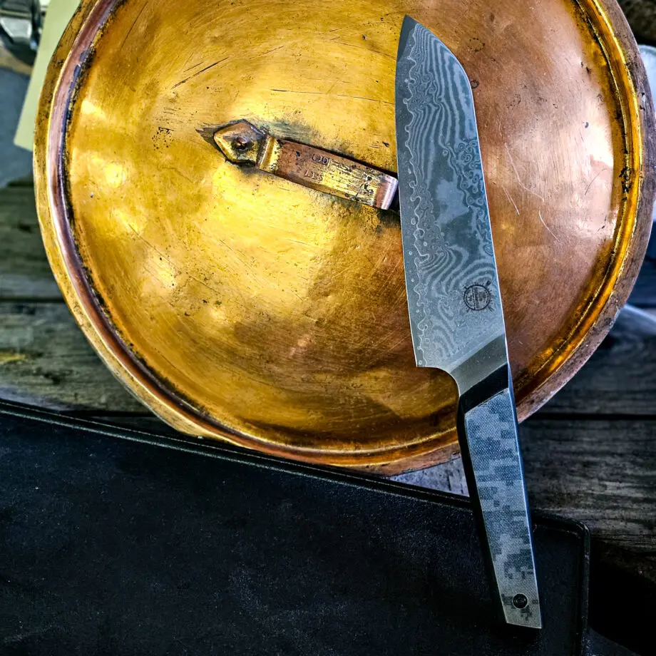 Kockkniv "Camo31 #2" - Santoku-varianten i BBQmonsters finaste knivserie. Rakbladsvasst blad med vacker damaskus mönster och coolt digi-camo-handtag En smidig, lättstyrd och inte minst vacker kockkniv - Camo31 #2 En santoku-kniv är något kortare än en klassisk kockkniv och har ett mer rundat avslut av eggen ovansida. Många använder santokuknivar till att skära upp och hacka grönsaker men kniven fungerar utmärkt även för kött. Introduktionspris - passa på! Bladet är vackert damaskusmönstrat - som helhet en av de vackraste knivar som vi sett och definitivt den vassaste - totalt 100% "intstagramvänlig" och photogenique. Vi gjorde ett test med den större kockkniven i samma serie: en liten plommontomat (ca 10 gram) släpptes från några decimeters höjd mot knivens egg och utan att studsa så skars tomaten i en fin skiva med endast tyngdlagens inverkan mot knivens egg - imponerande! Ibland kan man se liknande test men där man istället släpper något betydligt tyngre, som en mindre melon eller en banan...ett sådant test säger inte allt för mycket, men vårt test berättar att denna kniv skall behandlas med största försiktighet. Denna Santoku kockkniv är en perfekt present, julklapp eller farsdagspresent till dig själv eller någon annan som uppskattar matlagning. Kniven levereras i en svart presentbox med BBQmonsters logo och sigill. Total längd: 31 cm Längd på bladet: 18 cm Längd på skaftet: 13 cm Vi rekommenderar att du använder våra smidiga skyddshandskar när du använder denna kniv