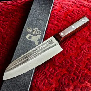 Santoku kockkniv Red Velvet #16 vacker kockkniv från BBQmonsters serie av Asiatiska kockknivar - liknande kniv säljs för det tredubbla på andra sidor! Söker du en serie av välarbetade och lättskötta kockknivar? Ta en kik på BBQmonsters egna serie knivar! Samtliga knivar i serien kommer i en svart presentförpackning med BBQmonsters sigill "Make BBQ great again" tryckt på locket. Knivarna från BBQmonster har även BBQmonsters logo ingraverad på bladet. Vi sätter bara vår logo på prylar som vi verkligen tycker om - detta är en sådan. Introduktionspris - passa på! En perfekt till grillnörden, en present till pappa på farsdag eller till dig själv helt enkelt! Santoku betyder "tre syften" på japanska och det berättar att detta är en kockkniv för både fisk, kött och grönsaker. Det lite kortare bladet gör att det är enkelt att arbeta med precision. Behöver du ett längre blad för att tranchera större stekar så ta en kik på Gyuto varianten i denna Red velvet serie. Bladet på denna Red Velvet #16 är vackert dekorerat med mjuka följsamma mönster inhamrat i stålet. Bladet har en perfekt balans mellan smidigt och robust. Eggen är extremt vass och lättskött. Varje blad är unikt i sitt utseende vilket tillsammans allts som allt gör detta kniven rejält "intstagramvänlig" och photogenique. Bladet är genomgående och avslutas med det snygga fyrkantiga handtaget som är av rött ädelträ och som har tre nitar av mässing. Skaftet ger ett skönt grepp och är enkelt att rengöra. Handtaget passar både höger- och vänsterhänta. Kolstål med blandning X50CrMoV15 Hårdhet 56° HRC vilket är ett relativt mjukt stål - något som gör att du själv enkelt kan hålla din kniv vass. Total längd: 30,5 cm Längd på bladet: 17,5 cm Längd på skaftet: 13cm Vikt: 234 gram