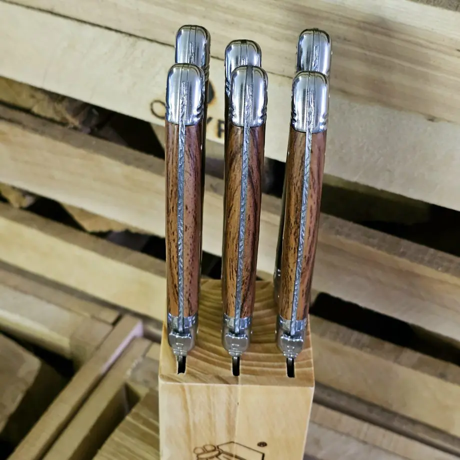 Köttknivar Laguiole Wood - 6pack köttbestick - eleganta bestick som skär snyggt kommer med vackert knivställ av trä Laguiole Wood köttknivar är lika fina att skära med som de är vackra att duka med. Du köper dessa i 6-pack och de kommer med ett vackert förvaringsställ av trä - de kan med andra ord stå framme utan att skämma ut sig. Här har du den perfekta presenten till dig själv eller en annan köttälskare som uppskattar både effektiva knivar att skära med och som gillar den eleganta och tidlösa designen som Laguiole står för. Laguiole Besticken har ett detaljerat och vackert handtag som ligger bra i handen. Handtag och knivblad har samma längd 12cm + 12cm, vilket ger knivarna en perfekt balans. Eggen är mycket fint tandad vilket gör att du utan problem skär fiber för fiber med raka snygga snitt. Dessa köttbestick bör diskas för hand även om de är klassade att tåla maskindisk (dock är maskindiskmedel ofta mer blekande och tärande på material med mycket detaljer - som dessa knivar har). I förpackningen ingår: 6 stycken eleganta Laguiole köttknivar 1 styck knivställ / knivblock i trä