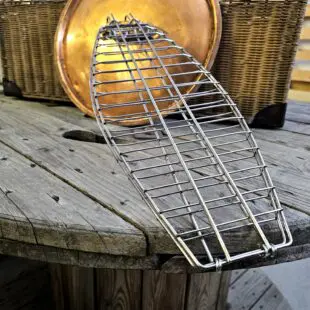 Fiskhalster Grillhalster med krok istället för handtag - passar med locket stängt - rostfritt stål Fiskhalster är ett grillhalster tänkt för hel fisk eller filéer. Fördelen blir enkel vändning utan att fisken går sönder eller bränner fast på gallret. Krok för vertikal rökning avslutar. Halstret ersätter grillnät med fördelen att du slipper teflonliknande material i din matlagning.  BBQmonsters Fiskhalster är konstruerat i formen av en fisk i storlek runt 2kg. Halstret öppnas och stängt enkelt med en ring som låser de båda sidorna. Innehållet i halstret skapa spänningen som krävs för att ringen skall låsa sig fast och utrymmet är naturligt flexibelt och tolererar en tjocklek på mellan 2 och 4 cm. Vill du grilla eller röka fisken så är det praktiskt att halstret inte har ett handtag, på så vis kan du utföra rökningen med stängt lock. Storleken gör att detta fiskhalster passar både i gasolgrillar, Kamado grillar som Kamado Joe classic och klotgrillar (och givetvis större modeller som Big Joe och offset smokers) Finns utrymmet till att hänga in fisken vertikalt är detta möjligt tack vare att halstret avslutas med en krok. För ännu säkrare förankring kan du först hänga in en slaktkrok och sen hänga halstret i denna. Fördelen med hängande rökning av fisk är att du förlänger tiden i rök, då luft leder sämre än galler (som fisken annars ligger på). Testa gärna kallröka lax och öring med en kallrökningsenhet, en spiral du fyller med spån och fjuttar fyr, utan att använda någon annan form av värmekällan.