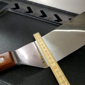 Grillspade - Flippa burgare Här har du en riktig klassiker. Du som har besökt korvkiosken på hörnet i den lilla staden har sett denna spade tidigare - en klassiker! Att många flipping-pros föredrar denna grillspade när de flippar burgare beror på den sköna svikten i stålet. Du kan lätt trycka stålet in under burgaren och därefter med en liten kick nedåt få burgaren att dansa runt i luften. Vem vet - det är kanske just du som slår igenom i "Talang" med detta vapen? Den användbara ytan är drygt 7 cm bred och 24 cm lång. Handtag av äkta trä och synliga nitar. Total längd ca 50cm