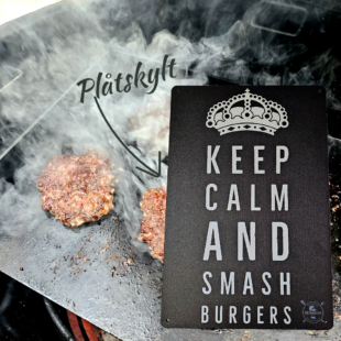 Plåtskylt / Tin sign med budskapet: keep calm and smash burgers. Given hos varje seriös burger-dude Skylt för kök, utekök, grillhörna, BBQ, Bar, Mancave Dekorera din favoritplats med skyltar och metalltavlor En tavla med de bevingade orden "Keep calm and smash burgers" Ja, det är ju gott, så varför inte? En perfekt skylt att hänga i uteköket och grillhörnan Tavlor i metall och plåtskyltar? BBQmonster har en häftig samling tavlor och skyltar i metall som kan vara den perfekta presenten eller tillbehöret till presenten som gör pricken över i:et, eller "the prick over the eye" som man säger i Amerikat... Metalltavlor för grill och BBQ är efterfrågade dekorer till utekök, mancaves och grillhörnor och med BBQmonsters uppsättning är chansen god att du hittar en skylt som passar just dig eller den person du skall köpa presenten till. Ett presenttips kan vara att om du köper låt säga ett paket spanska ginglas att då komplettera med en skylt som förstärker budskapet. Samma sak kan appliceras Ölglas, Kamados osv. Livsnjutare, Foodies och grillare är ofta glada för både god mat och god dryck. Därför kretsar många av dessa skyltar och metalltavlor på tema Mat, såsom recepttavlor (för exempelvis Pulled pork, Revben / Ribs och Brisket). Eller Dryck (whisky, bourbon, beer, öl, IPA, Cider, Stout och inte minst modedrycken GIN). Tavlorna i metall finns i ett antal olika format, men där det vanligaste är måtten 20 x 30 (stående) cm eller 30 x 20 (liggande). Det finns även ett par större modeller (bland annat runda). Skyltarna har en vikt kant så inga vassa kanter existerar. Hörnen är försedda med hål (på det fyrkantiga tavlorna) där du enkelt med två eller fyra spik eller skruvar fäster upp tavlan på underlaget. Du kan även använda dubbelhäftande tejp om det passar bättre mot underlaget. Keep calm and smash burgers! Du hittar alla tavlor och skyltar under kategorin Tavlor metall (www.bbqmonster.se/produkt-kategori/tavlor/)