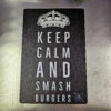 Plåtskylt / Tin sign med budskapet: keep calm and smash burgers. Given hos varje seriös burger-dude Skylt för kök, utekök, grillhörna, BBQ, Bar, Mancave Dekorera din favoritplats med skyltar och metalltavlor En tavla med de bevingade orden "Keep calm and smash burgers" Ja, det är ju gott, så varför inte? En perfekt skylt att hänga i uteköket och grillhörnan Tavlor i metall och plåtskyltar? BBQmonster har en häftig samling tavlor och skyltar i metall som kan vara den perfekta presenten eller tillbehöret till presenten som gör pricken över i:et, eller "the prick over the eye" som man säger i Amerikat... Metalltavlor för grill och BBQ är efterfrågade dekorer till utekök, mancaves och grillhörnor och med BBQmonsters uppsättning är chansen god att du hittar en skylt som passar just dig eller den person du skall köpa presenten till. Ett presenttips kan vara att om du köper låt säga ett paket spanska ginglas att då komplettera med en skylt som förstärker budskapet. Samma sak kan appliceras Ölglas, Kamados osv. Livsnjutare, Foodies och grillare är ofta glada för både god mat och god dryck. Därför kretsar många av dessa skyltar och metalltavlor på tema Mat, såsom recepttavlor (för exempelvis Pulled pork, Revben / Ribs och Brisket). Eller Dryck (whisky, bourbon, beer, öl, IPA, Cider, Stout och inte minst modedrycken GIN). Tavlorna i metall finns i ett antal olika format, men där det vanligaste är måtten 20 x 30 (stående) cm eller 30 x 20 (liggande). Det finns även ett par större modeller (bland annat runda). Skyltarna har en vikt kant så inga vassa kanter existerar. Hörnen är försedda med hål (på det fyrkantiga tavlorna) där du enkelt med två eller fyra spik eller skruvar fäster upp tavlan på underlaget. Du kan även använda dubbelhäftande tejp om det passar bättre mot underlaget. Keep calm and smash burgers! Du hittar alla tavlor och skyltar under kategorin Tavlor metall (www.bbqmonster.se/produkt-kategori/tavlor/)