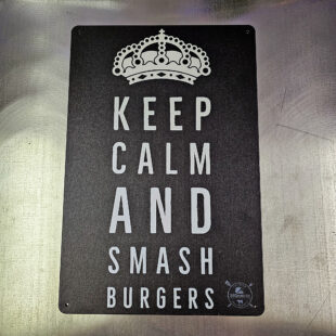 Plåtskylt / Tin sign med budskapet: keep calm and smash burgers. Given hos varje seriös burger-dude Skylt för kök, utekök, grillhörna, BBQ, Bar, Mancave Dekorera din favoritplats med skyltar och metalltavlor En tavla med de bevingade orden "Keep calm and smash burgers" Ja, det är ju gott, så varför inte? En perfekt skylt att hänga i uteköket och grillhörnan Tavlor i metall och plåtskyltar? BBQmonster har en häftig samling tavlor och skyltar i metall som kan vara den perfekta presenten eller tillbehöret till presenten som gör pricken över i:et, eller "the prick over the eye" som man säger i Amerikat... Metalltavlor för grill och BBQ är efterfrågade dekorer till utekök, mancaves och grillhörnor och med BBQmonsters uppsättning är chansen god att du hittar en skylt som passar just dig eller den person du skall köpa presenten till. Ett presenttips kan vara att om du köper låt säga ett paket spanska ginglas att då komplettera med en skylt som förstärker budskapet. Samma sak kan appliceras Ölglas, Kamados osv. Livsnjutare, Foodies och grillare är ofta glada för både god mat och god dryck. Därför kretsar många av dessa skyltar och metalltavlor på tema Mat, såsom recepttavlor (för exempelvis Pulled pork, Revben / Ribs och Brisket). Eller Dryck (whisky, bourbon, beer, öl, IPA, Cider, Stout och inte minst modedrycken GIN). Tavlorna i metall finns i ett antal olika format, men där det vanligaste är måtten 20 x 30 (stående) cm eller 30 x 20 (liggande). Det finns även ett par större modeller (bland annat runda). Skyltarna har en vikt kant så inga vassa kanter existerar. Hörnen är försedda med hål (på det fyrkantiga tavlorna) där du enkelt med två eller fyra spik eller skruvar fäster upp tavlan på underlaget. Du kan även använda dubbelhäftande tejp om det passar bättre mot underlaget. Keep calm and smash burgers! Du hittar alla tavlor och skyltar under kategorin Tavlor metall (www.bbqmonster.se/produkt-kategori/tavlor/)