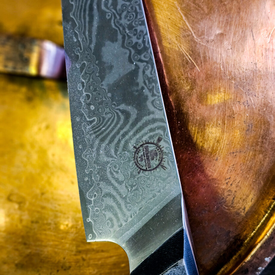 Kockkniv "Camo31 #2" - Santoku-varianten i BBQmonsters finaste knivserie. Rakbladsvasst blad med vacker damaskus mönster och coolt digi-camo-handtag En smidig, lättstyrd och inte minst vacker kockkniv - Camo31 #2 En santoku-kniv är något kortare än en klassisk kockkniv och har ett mer rundat avslut av eggen ovansida. Många använder santokuknivar till att skära upp och hacka grönsaker men kniven fungerar utmärkt även för kött. Introduktionspris - passa på! Bladet är vackert damaskusmönstrat - som helhet en av de vackraste knivar som vi sett och definitivt den vassaste - totalt 100% "intstagramvänlig" och photogenique. Vi gjorde ett test med den större kockkniven i samma serie: en liten plommontomat (ca 10 gram) släpptes från några decimeters höjd mot knivens egg och utan att studsa så skars tomaten i en fin skiva med endast tyngdlagens inverkan mot knivens egg - imponerande! Ibland kan man se liknande test men där man istället släpper något betydligt tyngre, som en mindre melon eller en banan...ett sådant test säger inte allt för mycket, men vårt test berättar att denna kniv skall behandlas med största försiktighet. Denna Santoku kockkniv är en perfekt present, julklapp eller farsdagspresent till dig själv eller någon annan som uppskattar matlagning. Kniven levereras i en svart presentbox med BBQmonsters logo och sigill. Total längd: 31 cm Längd på bladet: 18 cm Längd på skaftet: 13 cm Vi rekommenderar att du använder våra smidiga skyddshandskar när du använder denna kniv