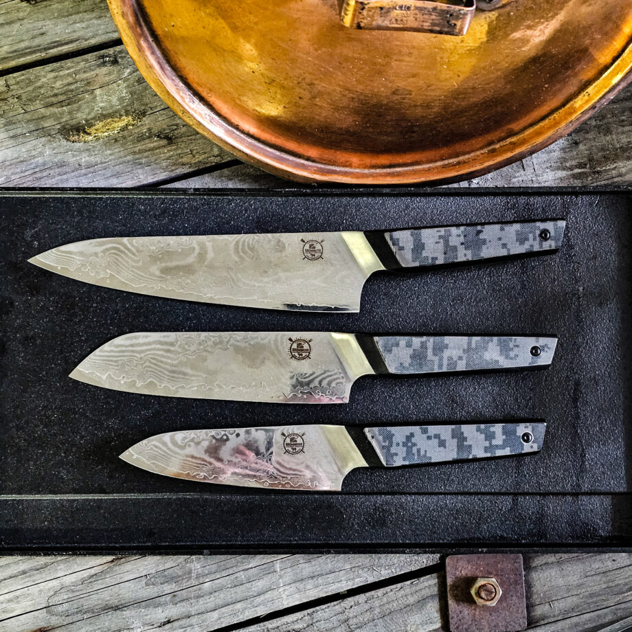 Kockknivs set "Camo" - tre knviar från BBQmonsters finaste knivserie. Rakbladsvassa blad med vackert damaskus mönster och coolt digi-camo-handtag Här har du det ultimata knivsetet, ett set med tre olika kockknivar som täcker alla behov i köket. Camo36 #1 En klassisk kockkniv som fungerar till allt i köket, både kött och grönsaker, detta då knivbladet är hela 27cm långt och precis som övriga knivar i denna serie - galet vassa! Camo31 #2 En santoku-kniv är något kortare än en klassisk kockkniv och har ett mer rundat avslut av eggen ovansida. Många använder santokuknivar till att skära upp och hacka grönsaker men kniven fungerar utmärkt även för kött. Camo27 #3 En Petty-kniv ("skalkniv") är betydligt kortare en klassisk kockkniv och något kortare än en Santoku-kniv Många använder Pettyknivar till finlir i köket och för att skära upp mindre grönsaker men kniven fungerar utmärkt även för att putsa kött. Introduktionspris - passa på! Bladet är vackert damaskusmönstrat - som helhet en av de vackraste knivar som vi sett och definitivt den vassaste - totalt 100% "intstagramvänlig" och photogenique. Vi gjorde ett test (se clipet på vår Youtube-kanal) med den större kockkniven i samma serie: en liten plommontomat (ca 10 gram) släpptes från några decimeters höjd mot knivens egg och utan att studsa så skars tomaten i en fin skiva med endast tyngdlagens inverkan mot knivens egg - imponerande! Ibland kan man se liknande test men där man istället släpper något betydligt tyngre, som en mindre melon eller en banan...ett sådant test säger inte allt för mycket, men vårt test berättar att denna kniv skall behandlas med största försiktighet. Detta kockkniv set med kockknivar är en perfekt present, julklapp eller farsdagspresent till dig själv eller någon annan som uppskattar matlagning. Knivarna levereras var och en i en svart presentbox med BBQmonsters logo och sigill. Total längd: 36cm / 31cm /27cm  Längd på bladet: 28cm / 18cm / 14 cm Längd på skaftet: 13 cm Vi rekommenderar att du använder våra smidiga skyddshandskar när du använder dessa knivar